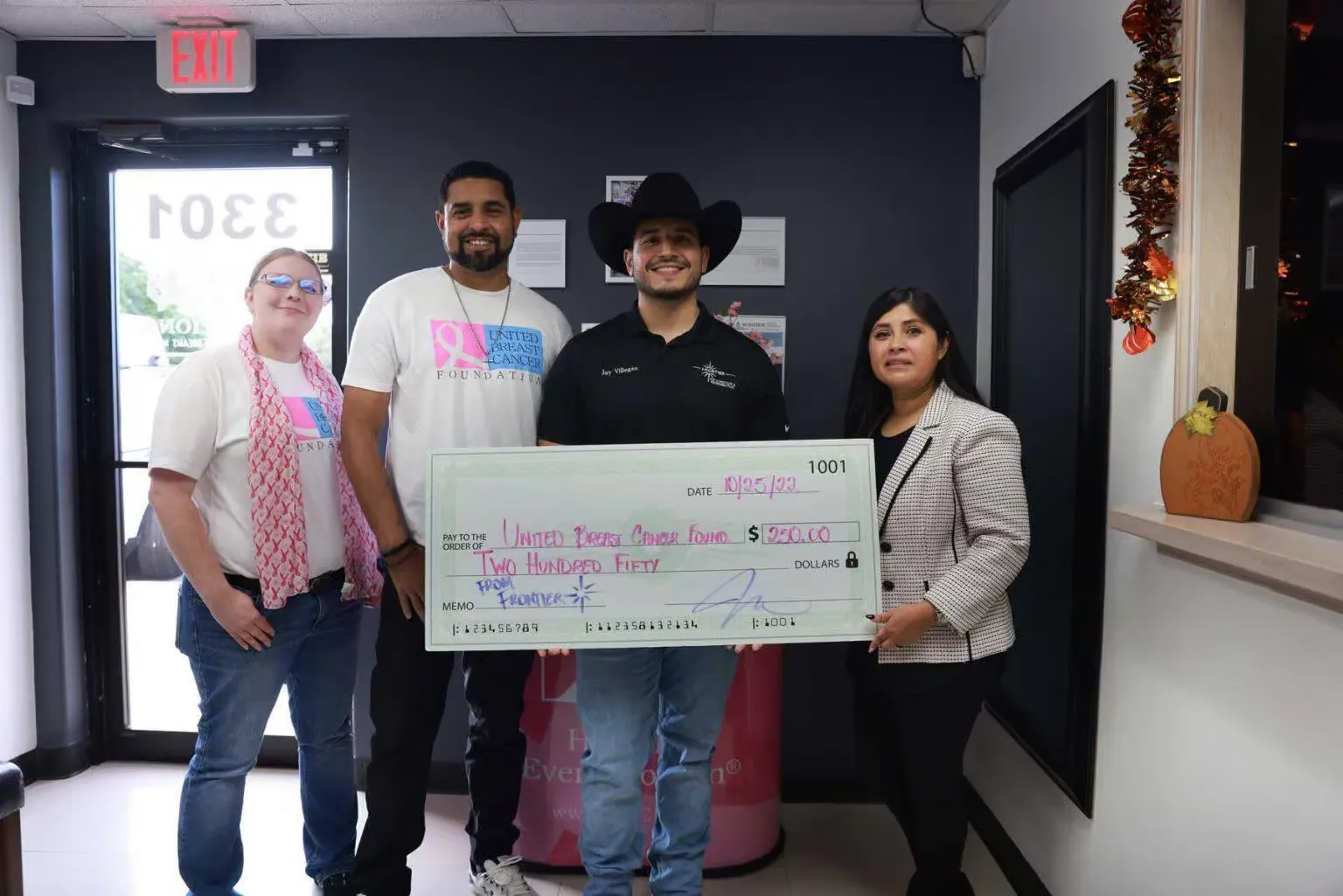Four people holding a large check indoors, likely a donation.