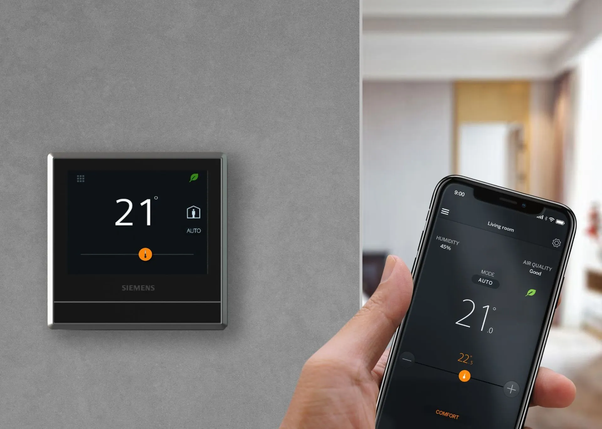 Thermostat on wall with display showing 21 degrees, person holding phone displaying same temperature.