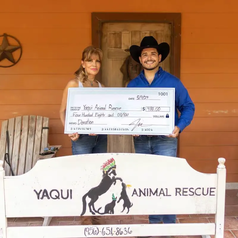 Two people holding a check for Yaqui Animal Rescue in front of a building.