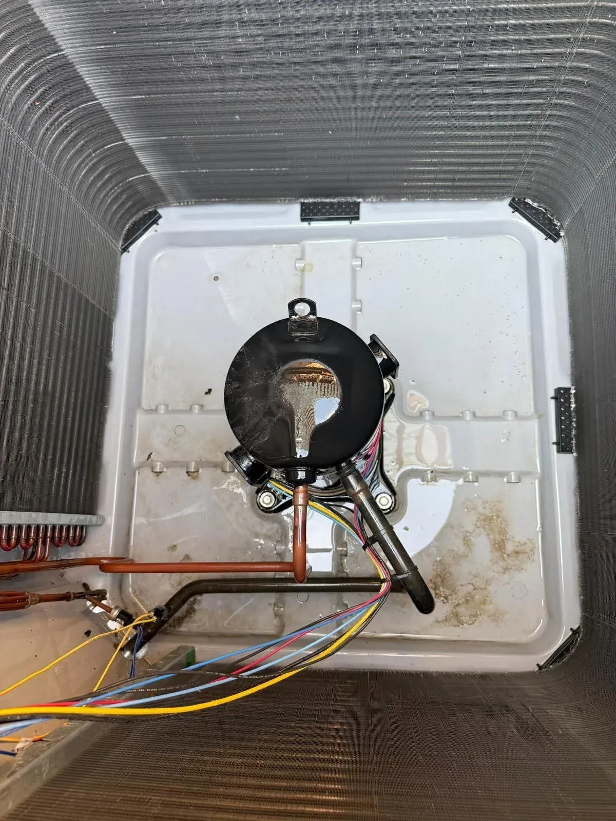 Open outdoor AC condenser with the fan removed, showing the compressor, refrigerant lines and wiring