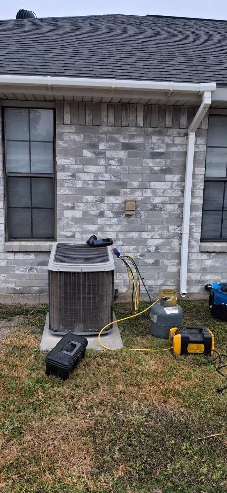 Outdoor AC condenser mid-install with a vacuum pump and refrigerant tank connected to the line set