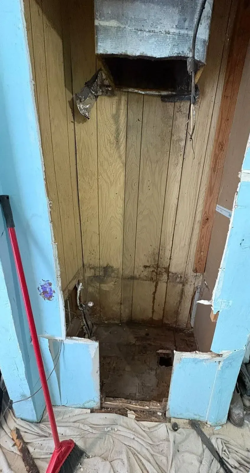 Empty air handler closet with water-damaged wood and a rusted plenum after the old unit was removed