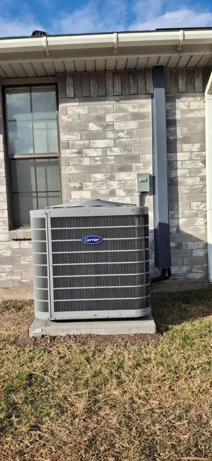 Carrier outdoor AC unit set level on a concrete pad next to a gray brick house