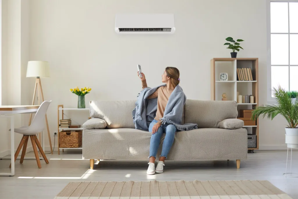 Woman on sofa using a remote to control an air conditioner in a bright living room.