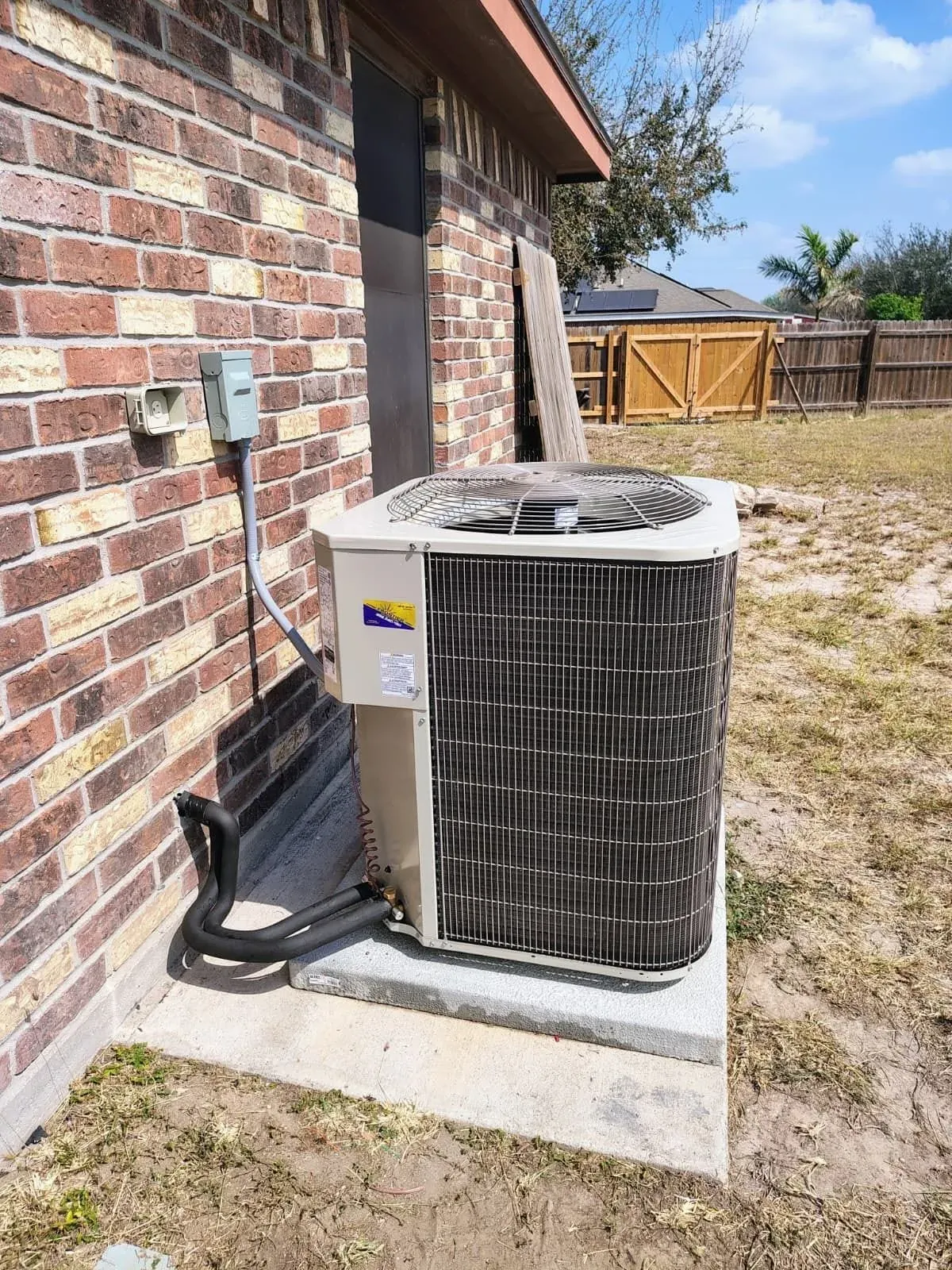 New outdoor AC condenser on a concrete pad beside a brick home after replacement