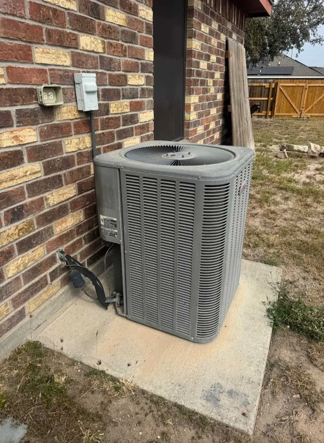 Worn outdoor AC condenser beside a brick home before replacement