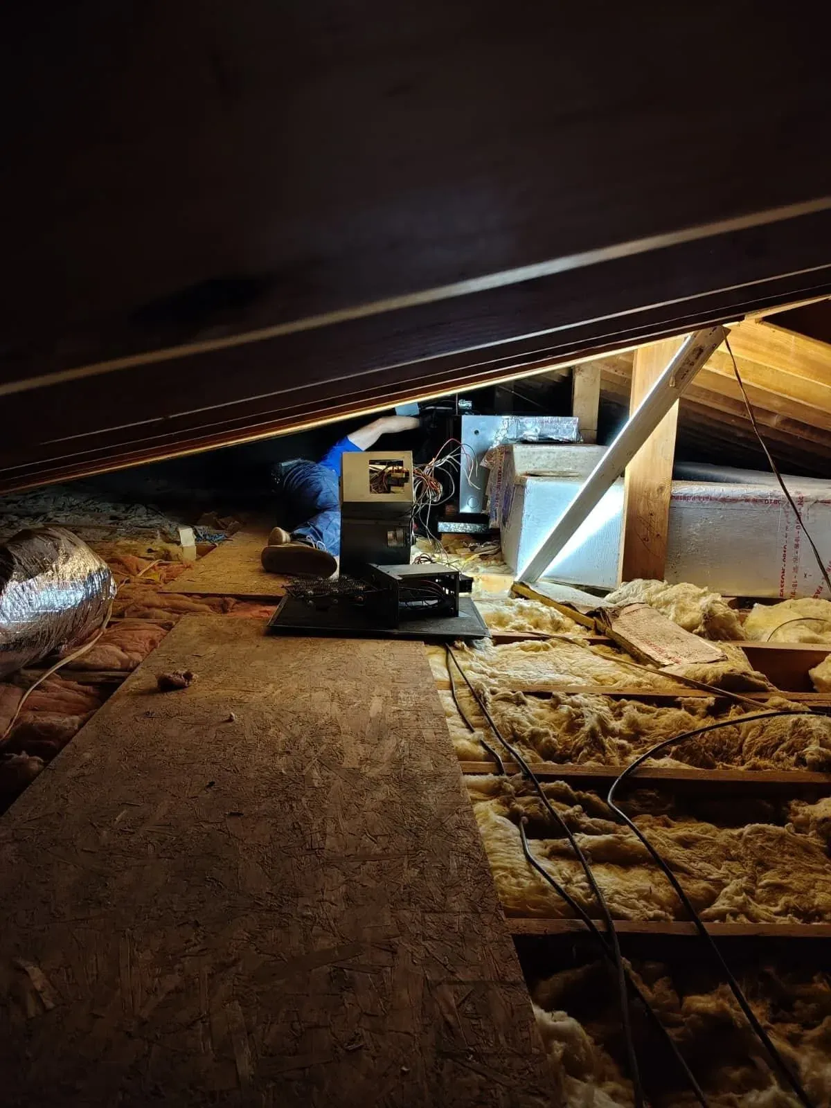 Technician servicing an air handler at the far end of an insulated attic